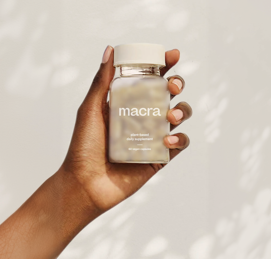 Hand holding a glass bottle labeled 'macra' against a neutral background