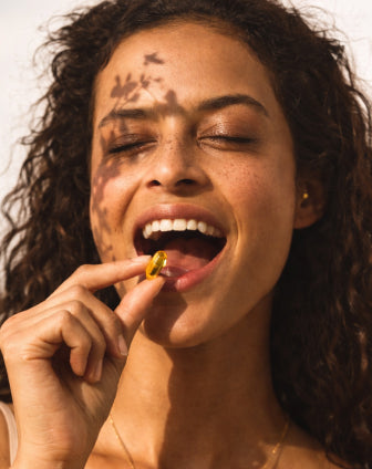 Woman with a gold earring and a small object in her mouth against a neutral background